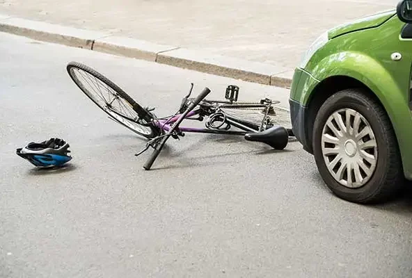 Bicycle and helmet lying in the road beside a green car