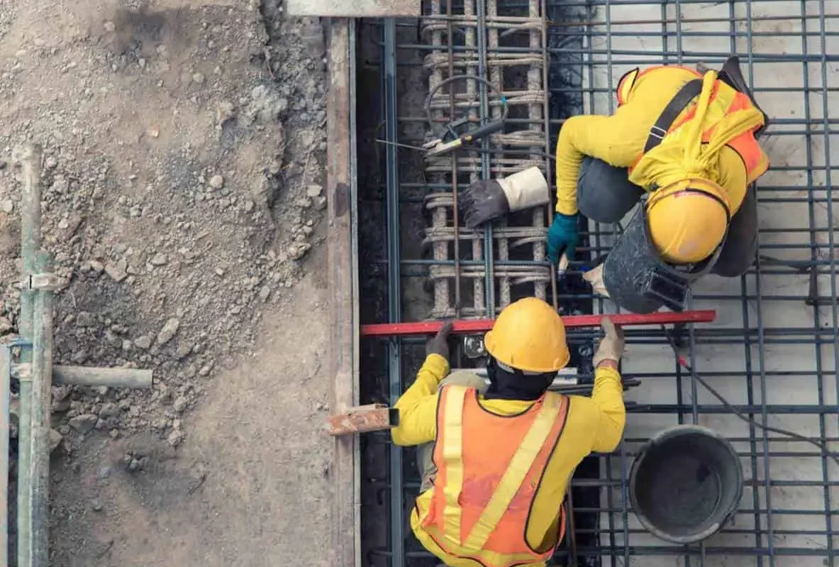 Two workers in hard hats and vests tying rebar on a building site