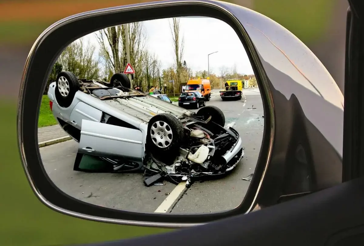 Overturned car on a roadside seen in a car wing mirror