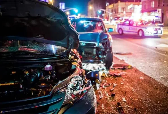 Damaged car with its bonnet open at a night crash scene with police lights