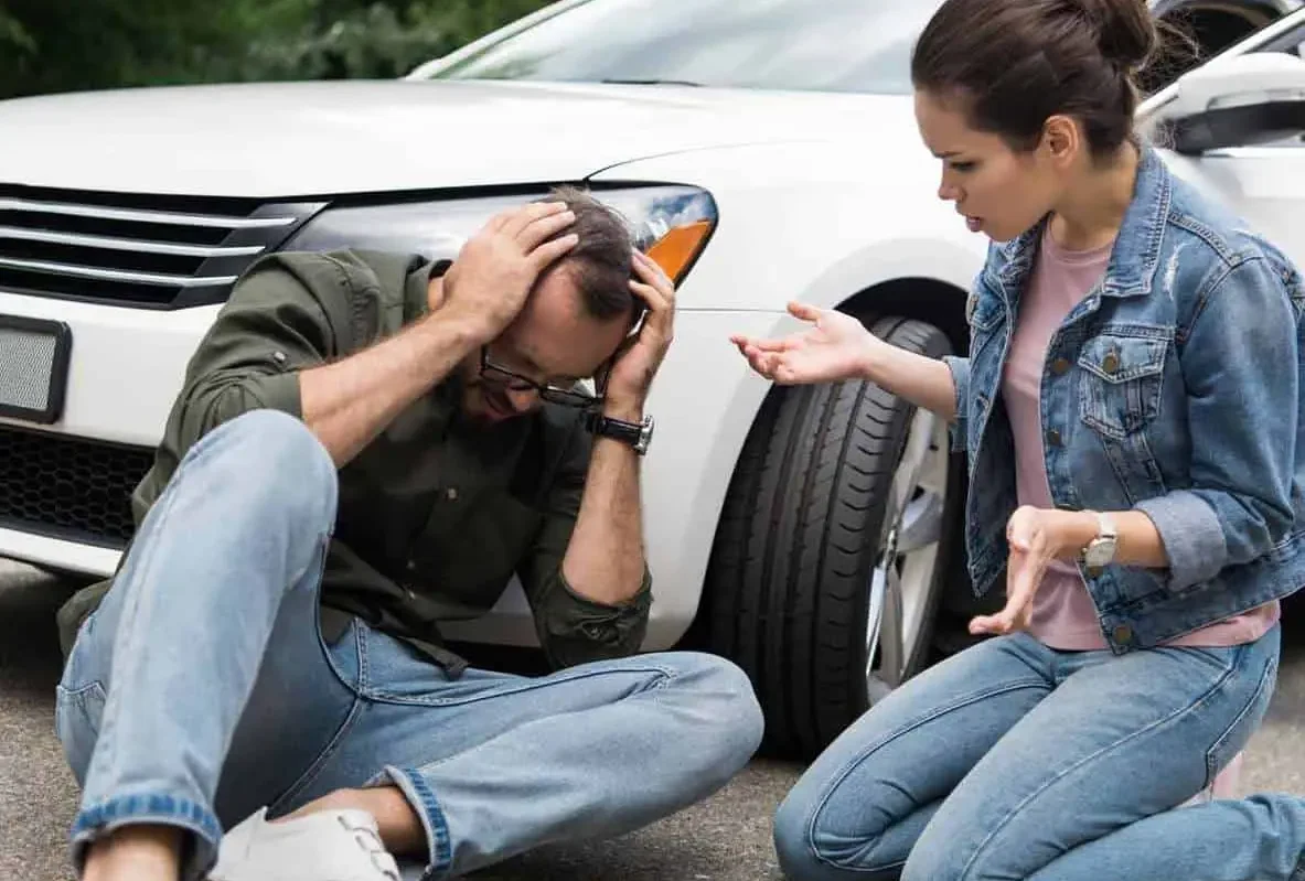 Man sitting on the road holding his head while a woman crouches beside him
