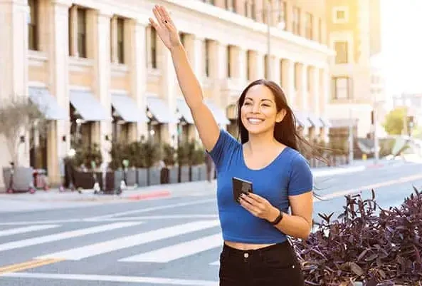 Woman with a phone raising her arm to hail a ride on a city street