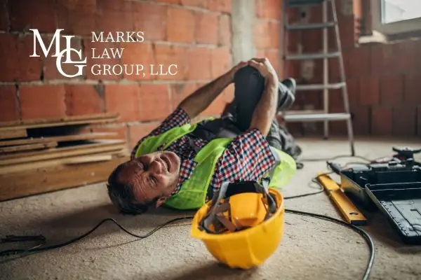 Construction worker in a hi-vis vest lying on the floor clutching his knee, hard hat beside him