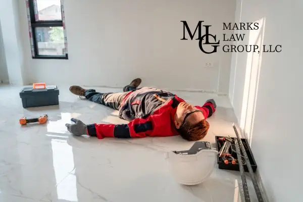 A construction worker lying on the floor beside a toolbox and hard hat after a fall