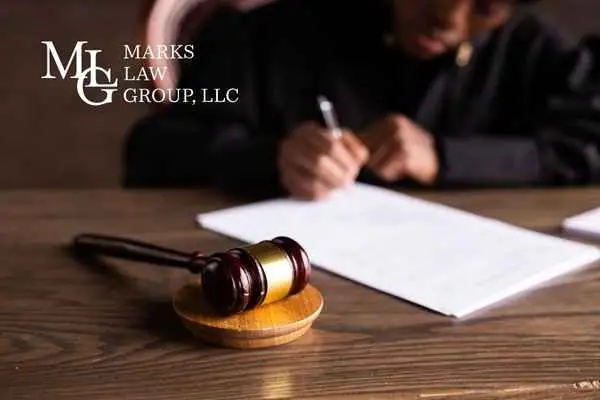 A gavel on a wooden desk with a person writing on papers behind it