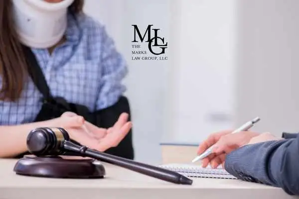 Woman in a neck brace and arm sling gesturing across a table to a note-taking adviser
