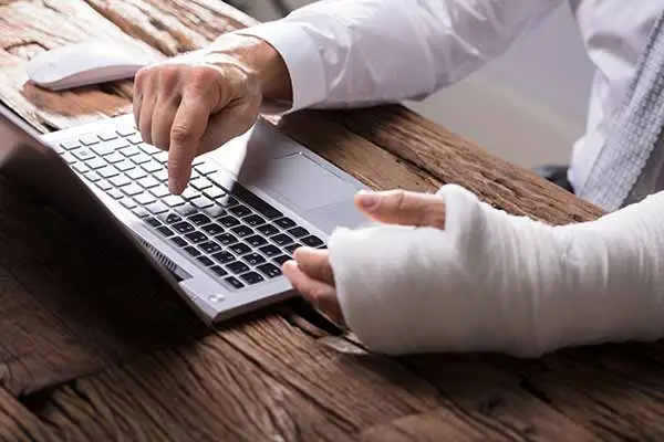 A man with a bandaged hand and wrist typing on a laptop
