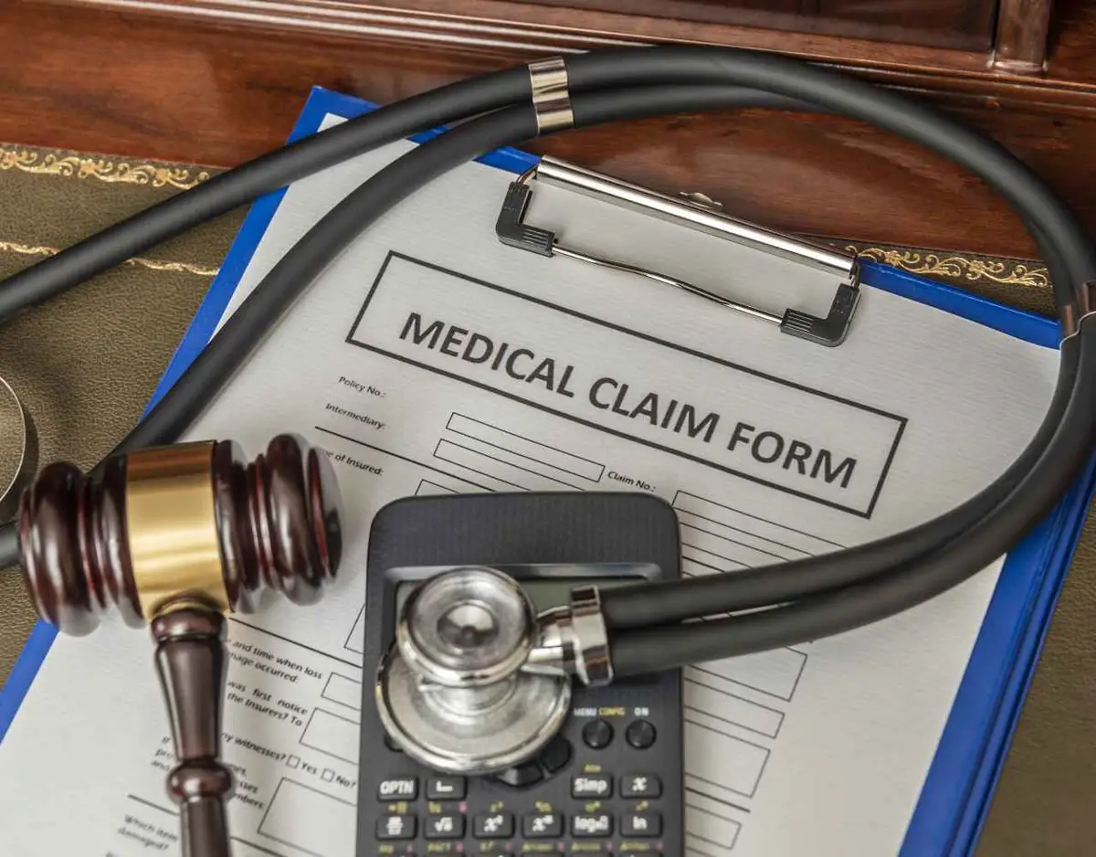 a clipboard with a medical claim form, gavel, stethoscope. and calculator on a desk