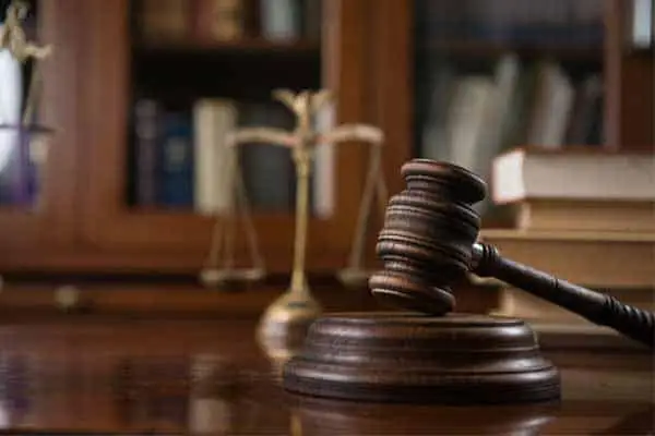 A wooden gavel on a desk with brass scales of justice and law books behind