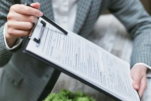 A person in a blazer holding out a clipboard with an insurance form and pen