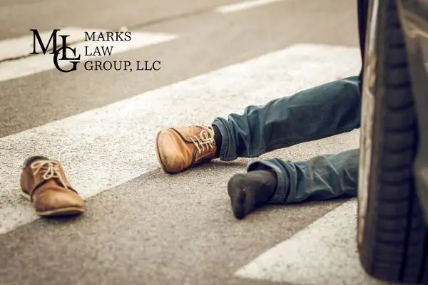 Legs of a person lying on a crosswalk beside a car tire, one shoe thrown off