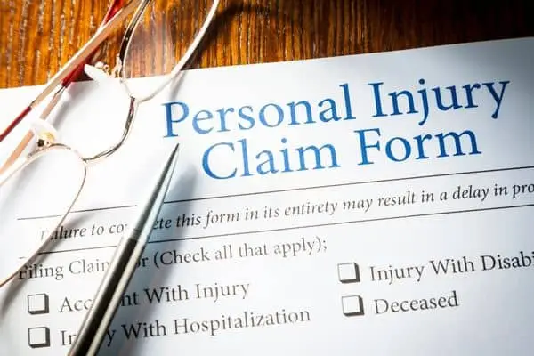 A Personal Injury Claim Form on a desk with reading glasses and a pen