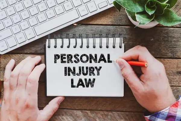 Hands writing Personal Injury Law on a notepad beside a keyboard