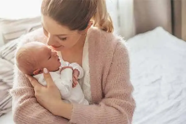 A mother in a pink cardigan cradling a sleeping newborn