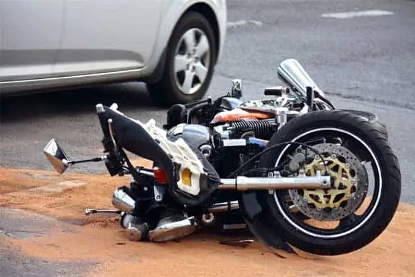 A motorcycle lying on its side on the road in front of a car