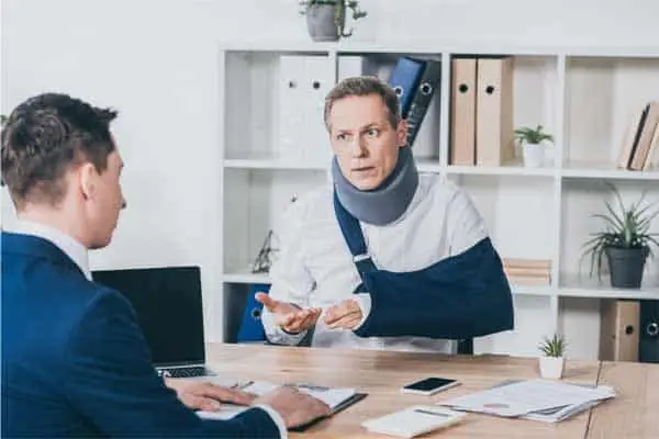 Man in a neck brace and arm sling talking with a lawyer at a desk