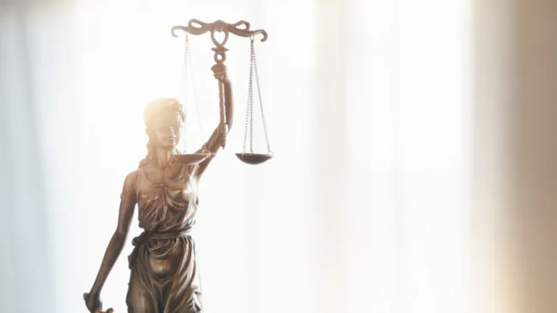 Bronze Lady Justice statue holding scales in front of a bright window