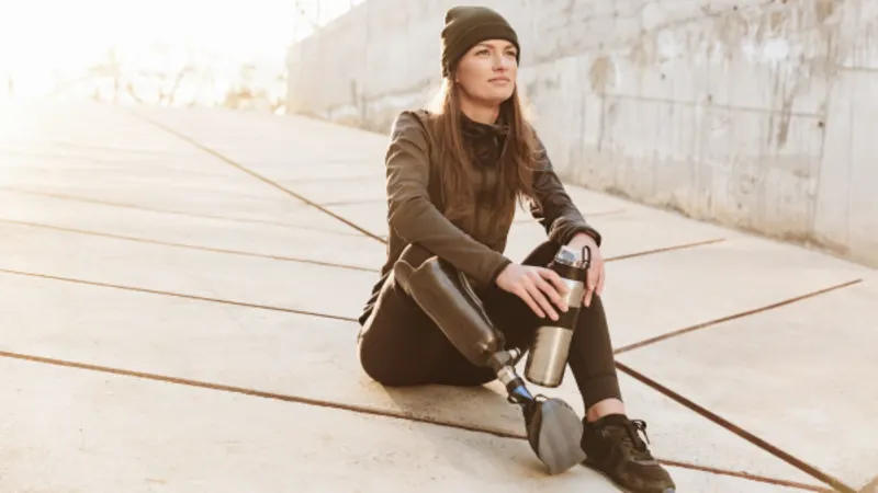 Young woman with a prosthetic leg sitting on pavement in low evening sun
