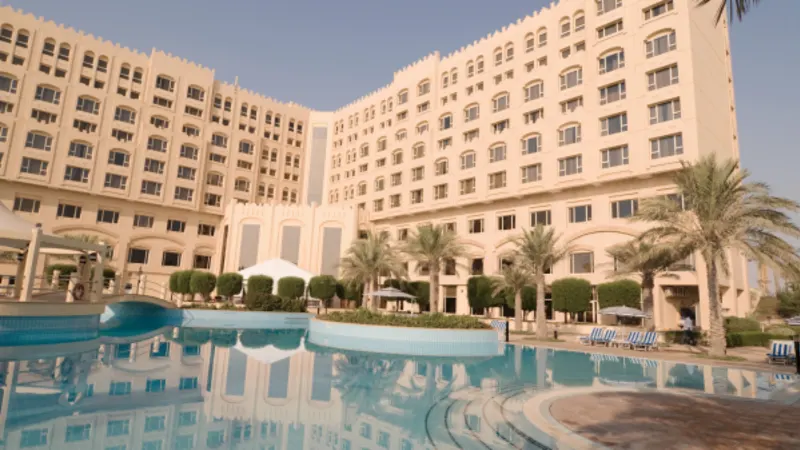 Large hotel building behind an outdoor swimming pool lined with palm trees