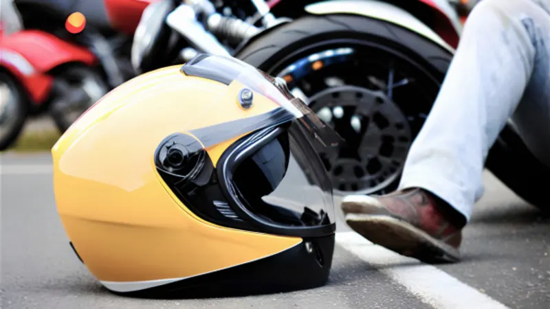 Yellow motorcycle helmet lying on the road beside a fallen bike and rider