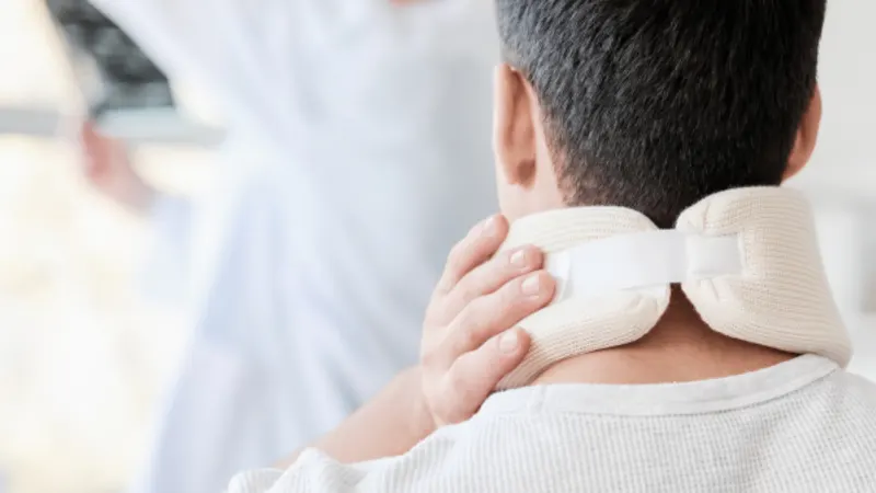 Man in a padded cervical collar holding his neck while a doctor reviews scans