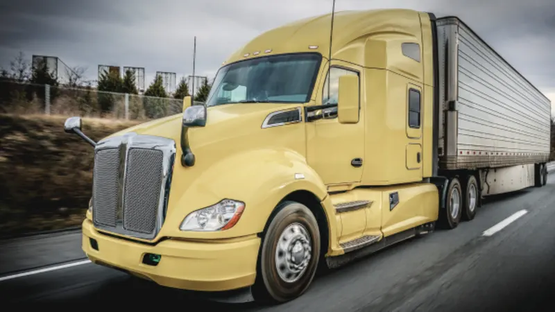 Yellow semi truck pulling a white trailer along a highway