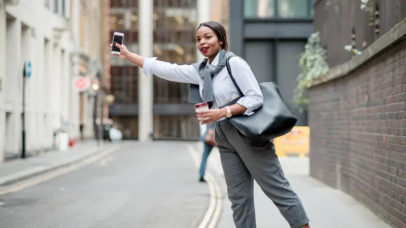 Woman on a city street raising her phone to hail a ride