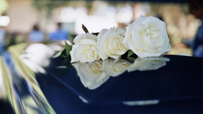 White roses resting on the polished dark lid of a coffin
