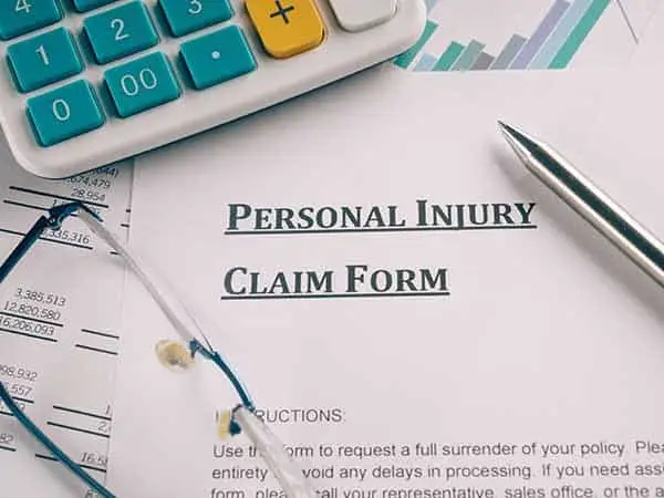 A personal injury claim form on a desk with a calculator, pen and glasses