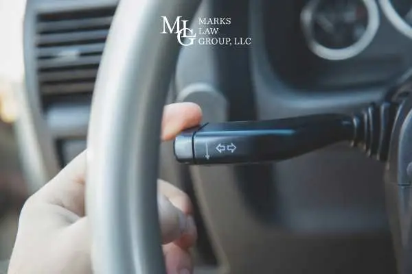 A driver's hand pushing the turn signal stalk behind the steering wheel