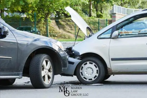 Two cars locked together after a head-on collision, one hood popped open