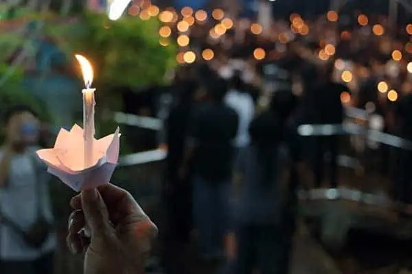 A hand holding a lit candle in a paper holder at a nighttime vigil