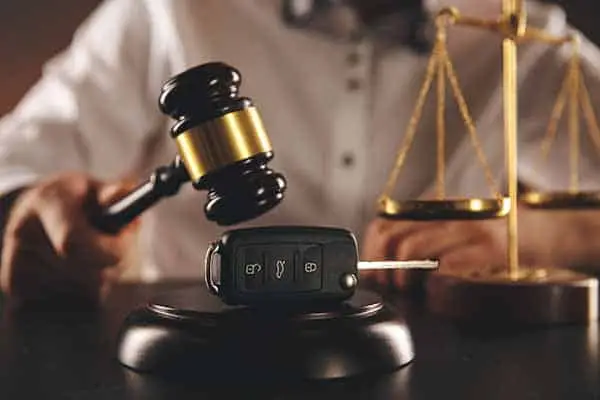 A car key fob under a gavel on a desk beside scales of justice