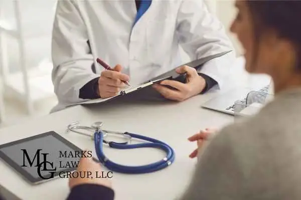 Doctor in a white coat writing on a clipboard opposite a patient, stethoscope on the desk