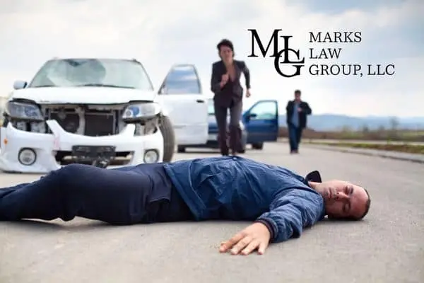 A man lying face down on the road as people run from a wrecked white SUV