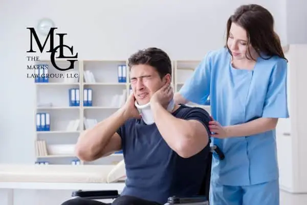 A man in a neck brace wincing in a wheelchair as a nurse steadies him