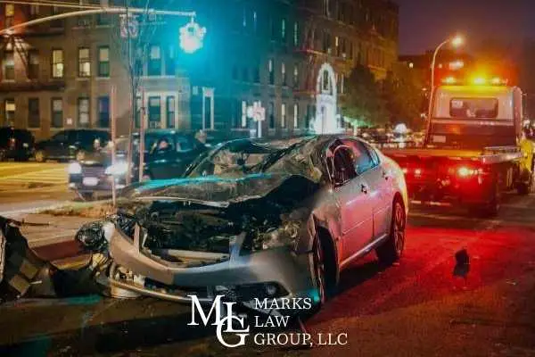 Wrecked car with a crushed front end beside a tow truck at night