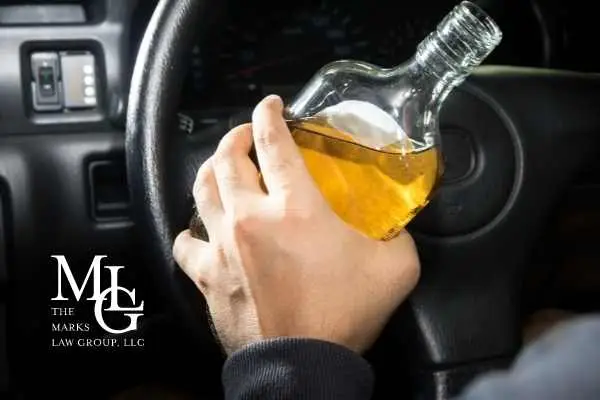 A driver gripping the steering wheel while holding a bottle of liquor