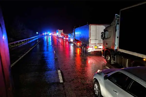 Trucks and cars stopped on a wet highway at night under emergency lights