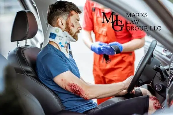 A bloodied driver in a neck brace being treated by a paramedic in the car