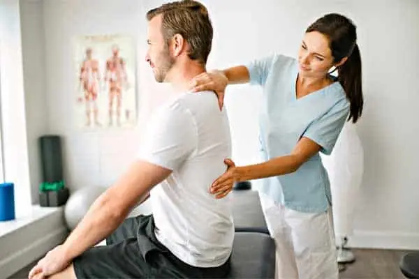 physical therapist in scrubs adjusting a seated man's shoulder and back