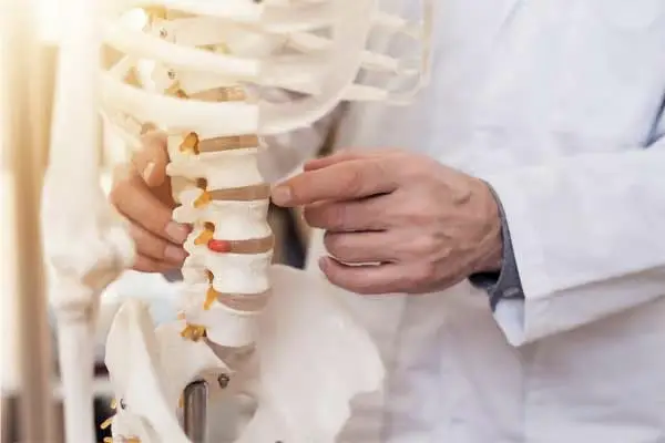 A clinician pointing at the lumbar vertebrae of a skeleton model, one disc marked red