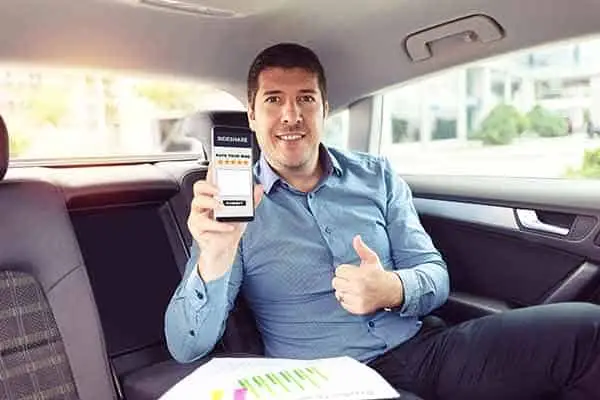 A back-seat passenger holding up a phone with a rideshare app and giving a thumbs up