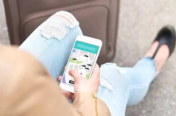 A seated traveler with a suitcase holding a phone showing a rideshare map