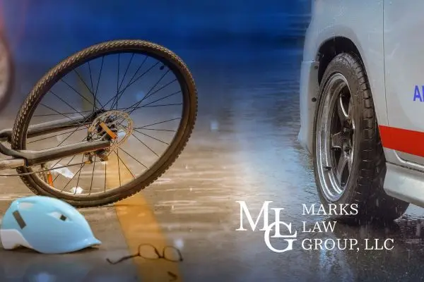 A bicycle and cracked helmet lying on wet pavement beside an emergency vehicle