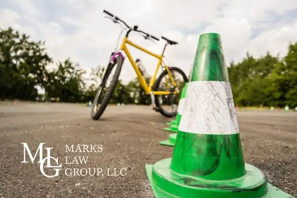A yellow bicycle parked behind a row of green traffic cones on asphalt