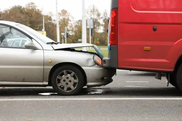 Silver sedan with a crushed front end wedged against the rear of a red van