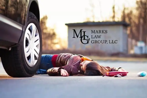 A woman lying on the pavement beside the front wheel of a stopped car