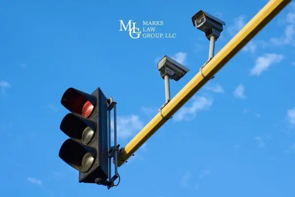 two cameras and a red signal light on a yellow pole against blue sky
