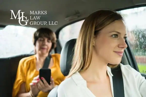 Young woman driving while an older passenger checks her phone in the back seat
